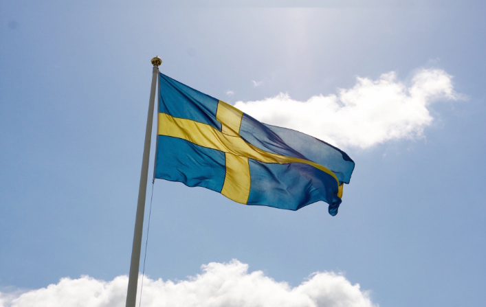 Sveriges flagga vajar mot en blå himmel med några vita moln.