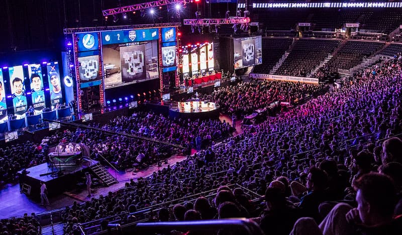 Stor publik tittar på en e-sportturnering i en arena med stora skärmar och färgglada ljus.