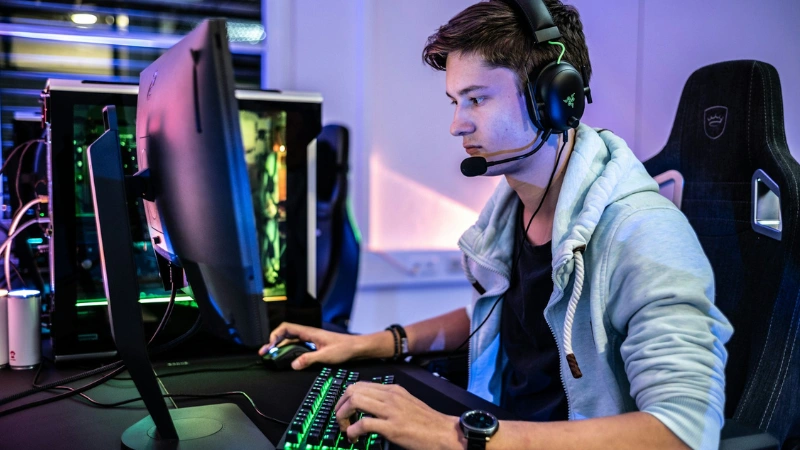 Person sitter vid dator och spelar datorspel med headset och mekaniskt tangentbord.