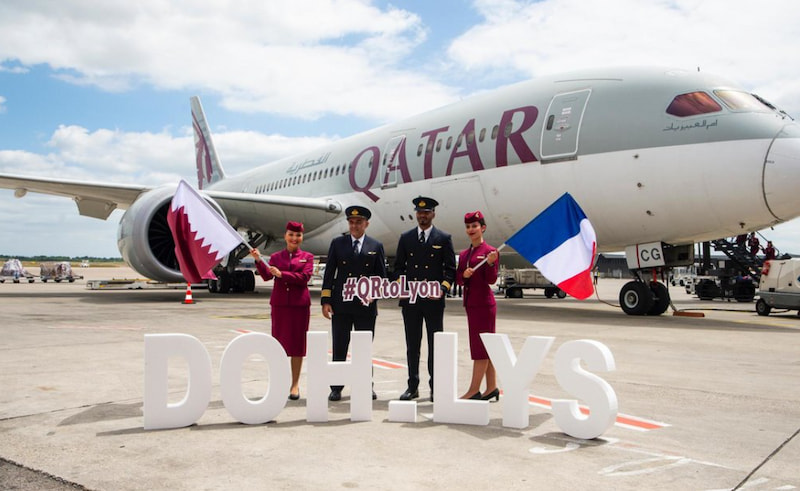 Fyra personer framför ett Qatar Airways-plan, två håller flaggor från Qatar och Frankrike, text "DOH.LYS" på marken.