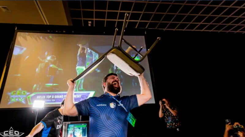 En person firar seger på e-sportturnering och lyfter en stol över huvudet på scenen under en finalmatch
