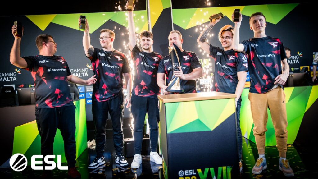 A group of esports players celebrate a victory, holding trophies and raising their arms in excitement amidst confetti and sparks.