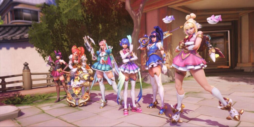 Seven colorful characters in ornate costumes pose together in a vibrant outdoor setting, showcasing playful expressions and accessories.