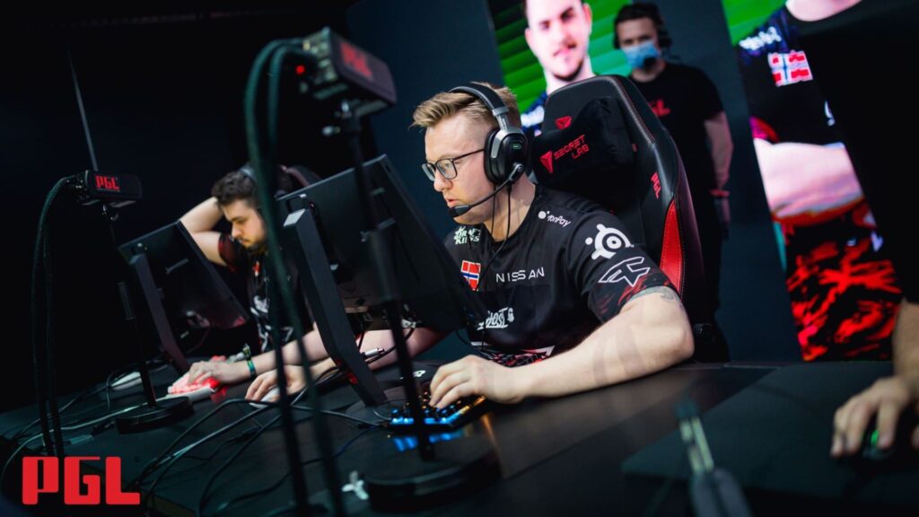 Esports players compete intensely in a dark arena, focused on their screens with gaming gear and vibrant LED lights in the background.