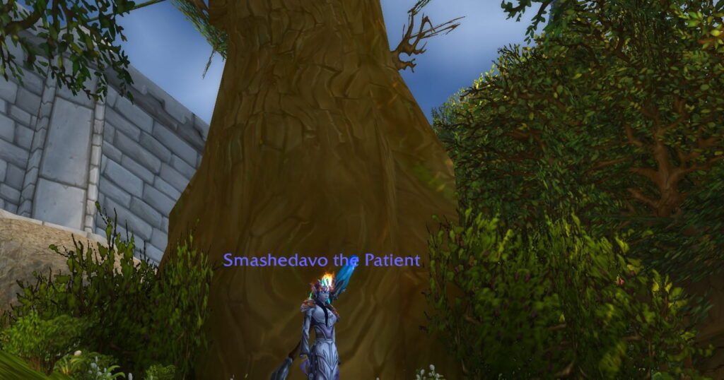 World of Warcraft character named Smashedavo the Patient standing beside a large tree near a stone wall, surrounded by foliage.