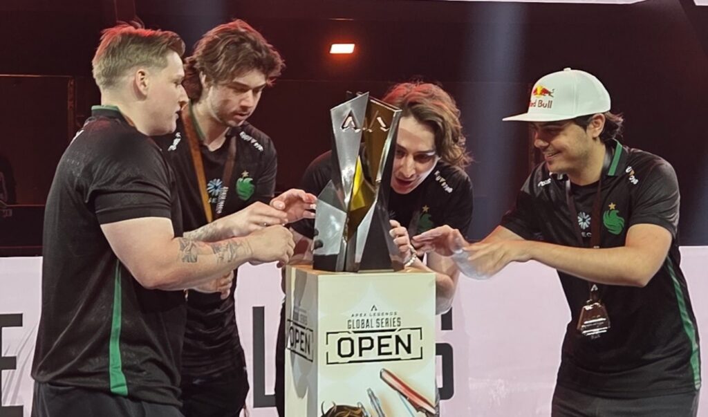 Four esports players celebrating around the ALGS Open trophy on stage, wearing black team jerseys, with one player in a white Red Bull cap, during the Apex Legends Global Series event in New Orleans.