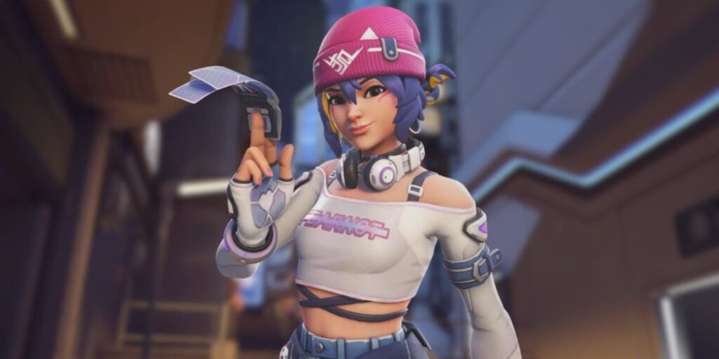 A character from Overwatch with blue hair wearing a pink beanie and headphones poses confidently, holding a gadget against a futuristic backdrop.