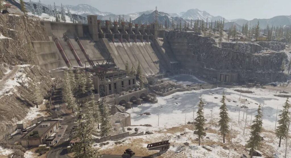 A panoramic view of a large dam surrounded by snowy mountains and pine trees, showcasing industrial structures and a frozen landscape.