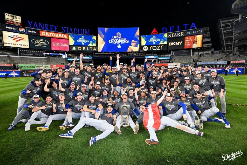 A jubilant baseball team celebrates their World Series championship at Yankee Stadium, holding a trophy amidst joyful poses and expressions.