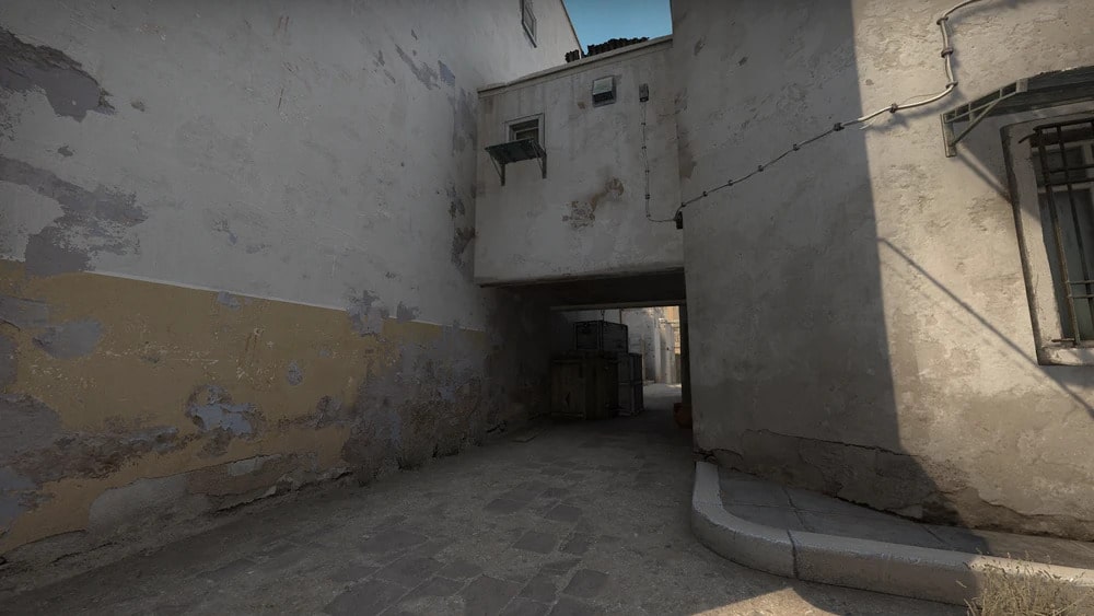 Mid overhang on Dust 2 in Counter-Strike: Global Offensive, showing a narrow alley with a covered passage, worn walls, and stacked crates under the archway.