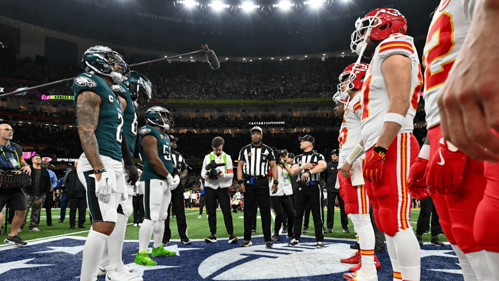 A football coin toss at the Super Bowl, featuring players from the Eagles and Chiefs, surrounded by officials and team staff.