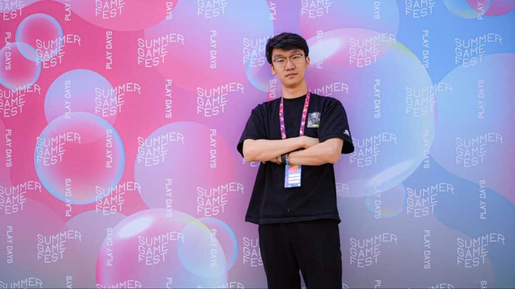 Xin Chang, Creative Director and Producer at Bad Guitar Studio, stands with arms crossed in front of a vibrant Summer Game Fest Play Days backdrop