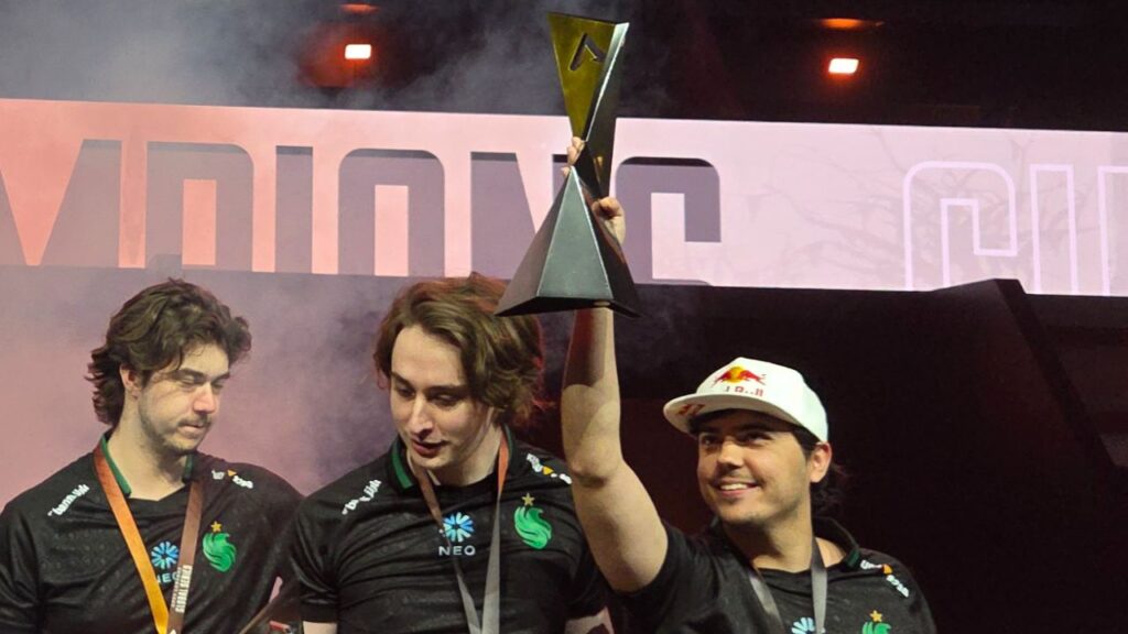 ImperialHal holding up the ALGS trophy in celebration alongside his teammates on stage, all wearing team jerseys and medals, with “CHAMPIONS” displayed in the background.