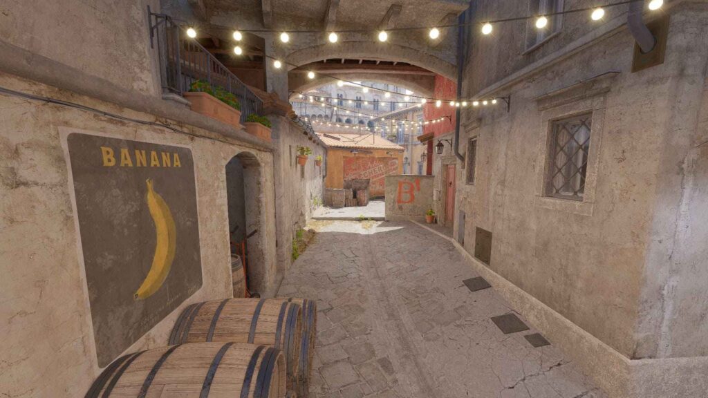 A charming cobblestone alleyway adorned with string lights, featuring a banana mural and wooden barrels on the sidewalk.