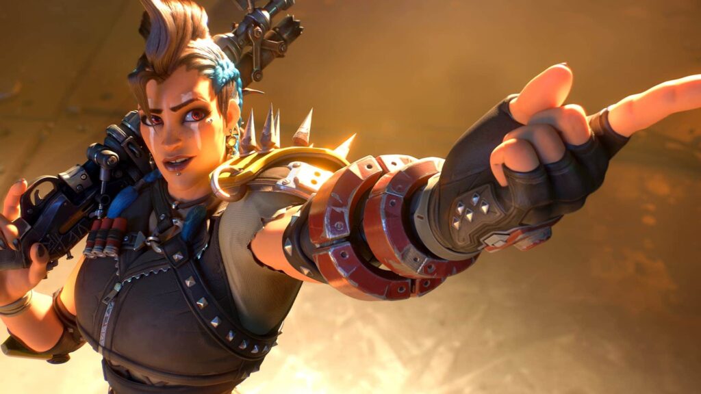Junker Queen from Overwatch pointing forward with a confident expression, wearing spiked armor and holding her shotgun over her shoulder.