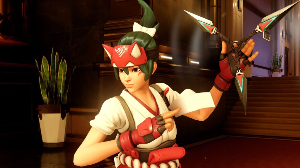 Kiriko from Overwatch 2 in a white and red outfit holding a kunai, standing in an indoor environment with stairs and plants in the background