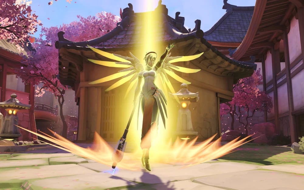 Mercy activates her Resurrect ability in Overwatch 2, glowing with golden light in a cherry blossom courtyard.