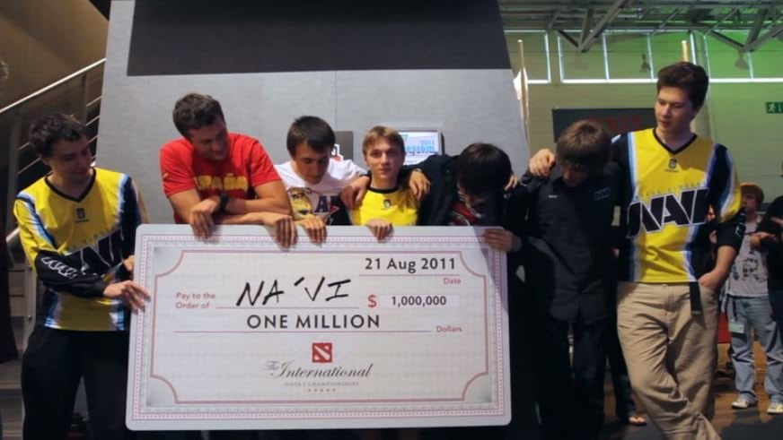 Team Natus Vincere (Na'Vi) celebrating their victory at The International 2011, holding a giant check for $1,000,000 awarded for winning the first-ever Dota 2 championship.