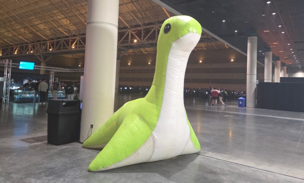 Large green and white inflatable Nessie mascot placed near a pillar inside a gaming event hall at the ALGS Open 2025