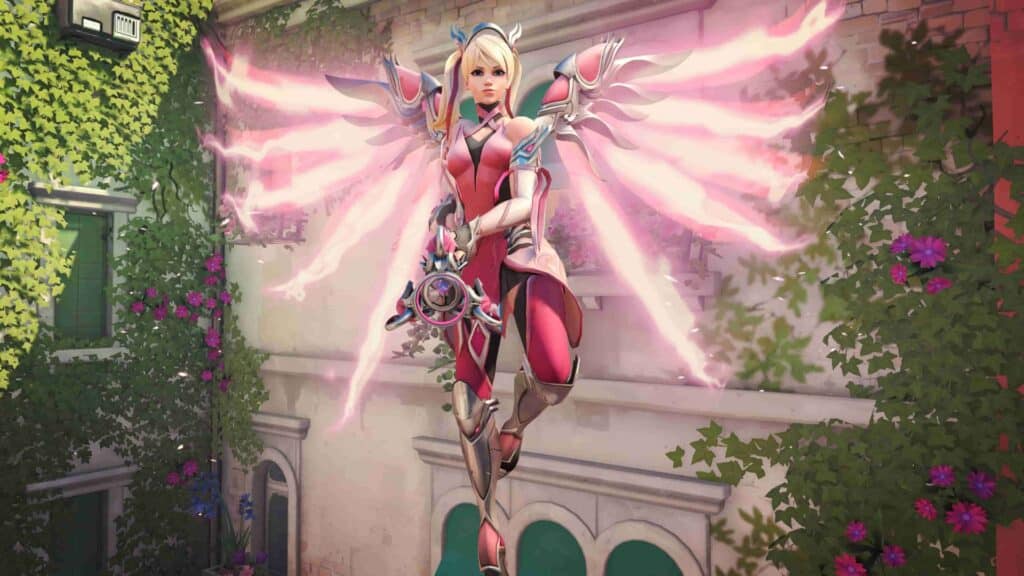 Overwatch 2’s Pink Mercy skin with glowing wings, shown mid-air against a flowery wall.