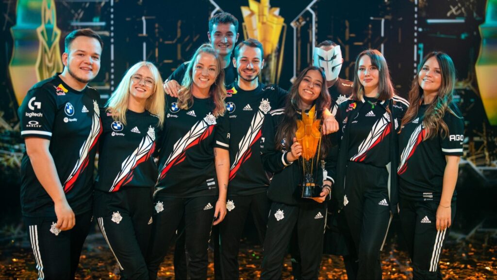 A group of esports competitors Faclons Vega in matching black jerseys pose proudly with a trophy, celebrating their victory on a vibrant stage.