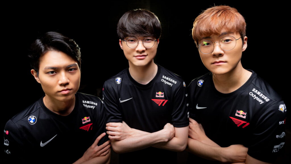 Three professional esports players from team T1 posing in black team jerseys with sponsor logos, standing confidently against a dark background.