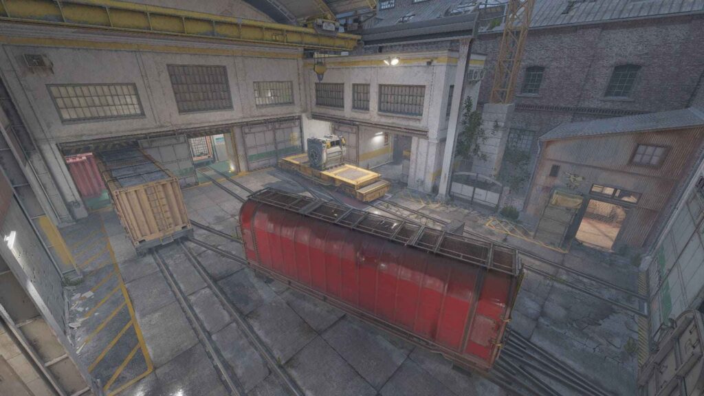 An overhead view of an industrial warehouse with train tracks, a red cargo car, and machinery under dim lighting.