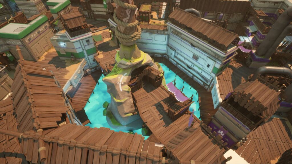 Aerial view of a colorful, wooden village with a central rock formation and turquoise water, showcasing various wooden pathways and buildings.