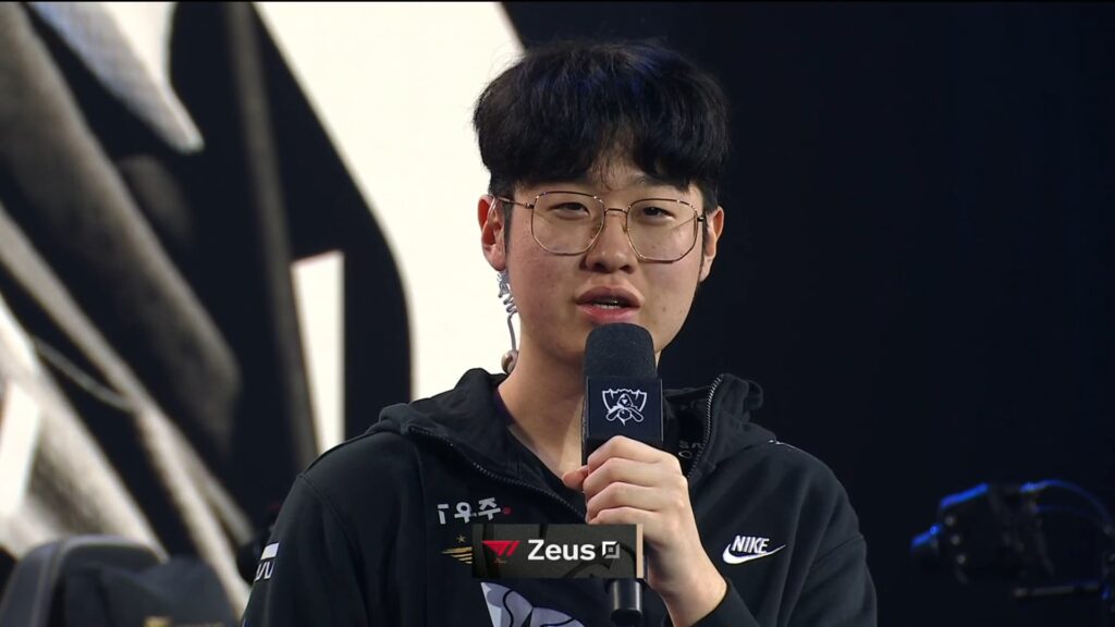 Zeus from T1 being interviewed on stage, holding a Worlds-branded microphone and wearing a black Nike team hoodie.