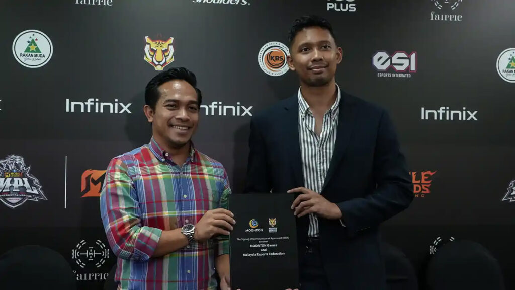Malaysia esports. Image of Muhammad Naim- Al-Amin and Fikri Rizal Mahruddin standing in front of backdrop holding contract