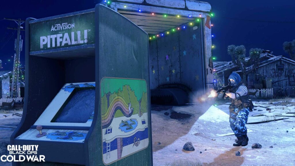 Soldier firing in snowy Nuketown map in Call of Duty: Black Ops Cold War, next to a Pitfall arcade machine and holiday lights