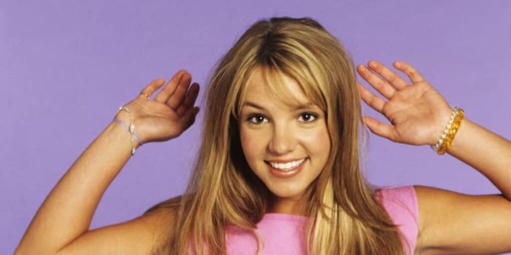 Britney Spears smiles widely, raising their hands playfully next to their head
