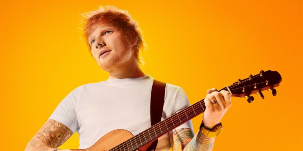 Ed Sheeran playing an acoustic guitar against a vibrant orange background