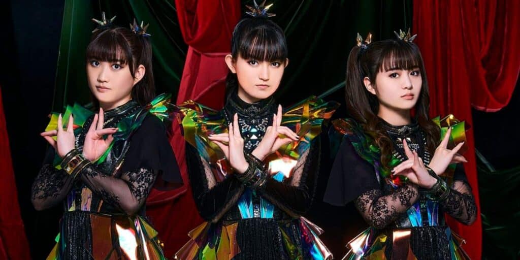 BABYMETAL's members stand in futuristic outfits with iridescent details and intricate lace sleeves