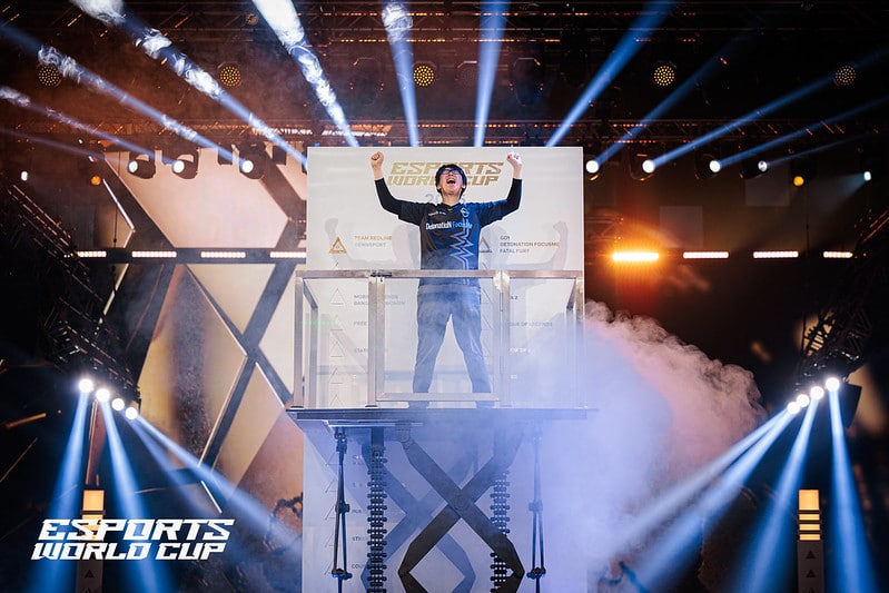 Esports World Cup winner stands on a lift, arms raised in triumph