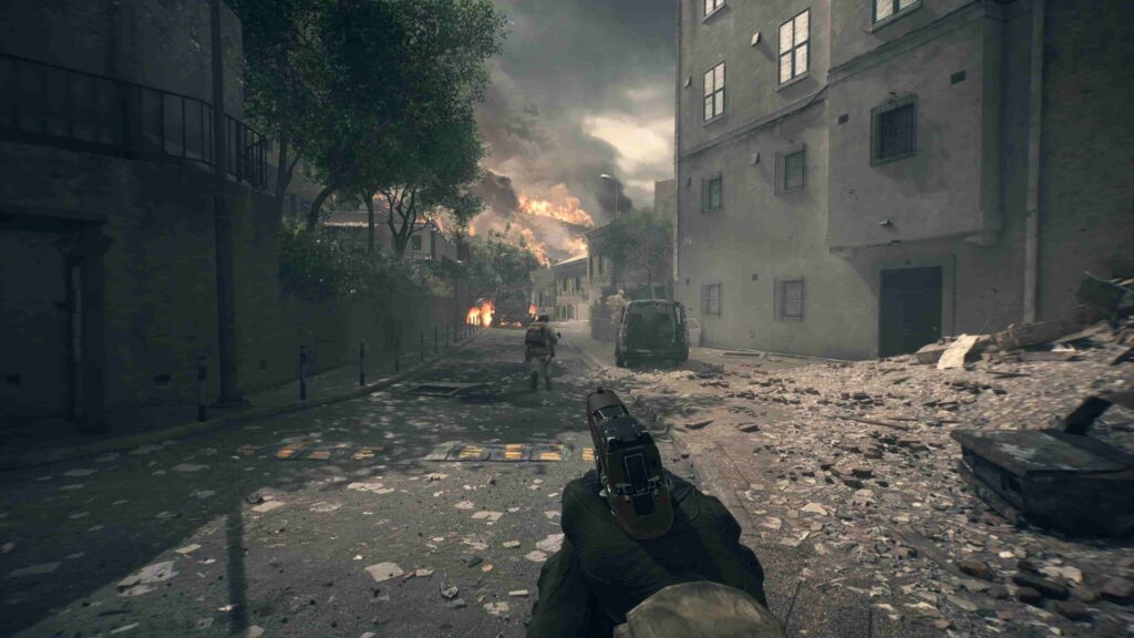 First-person view of a soldier holding a handgun in a war-torn street. There are burning buildings, debris, and smoke