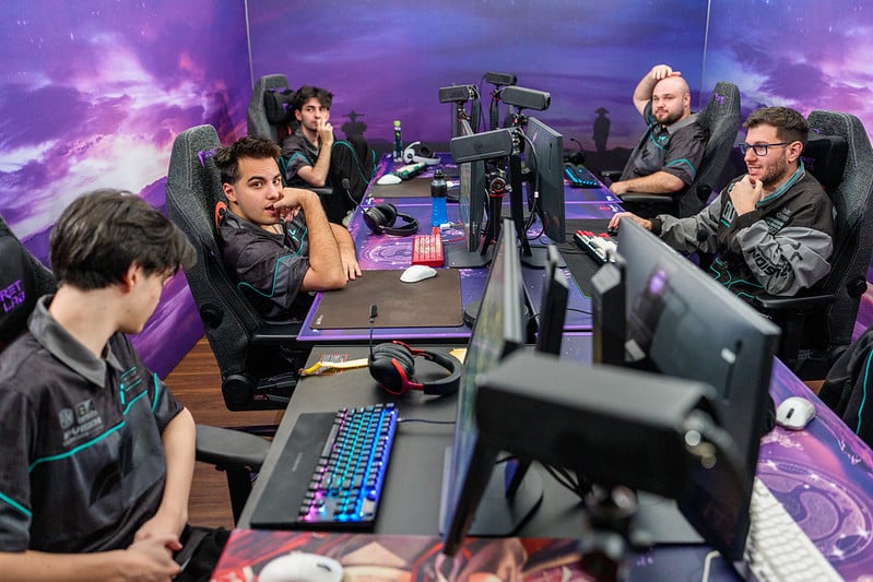 Fünf Personen in einem Spielraum sitzen auf Computern mit leuchtenden Tastaturen und erscheinen fokussiert und entspannt