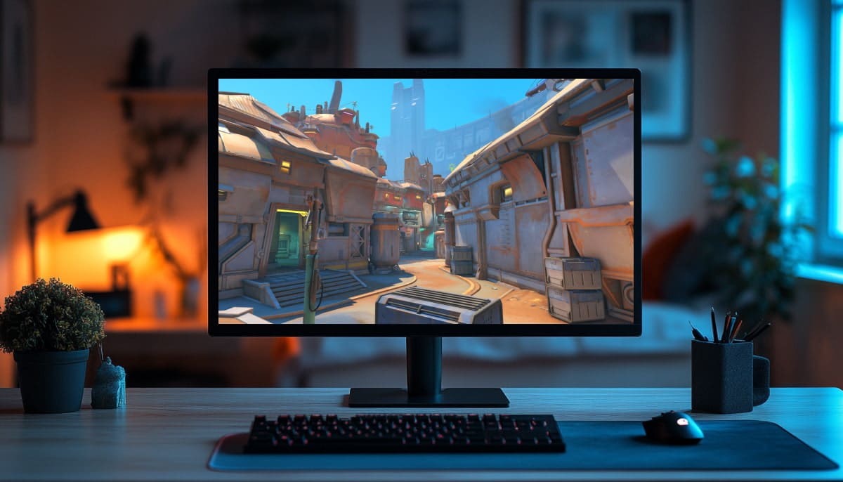 A computer on a desk shows a vibrant desert-themed video game with sandy buildings
