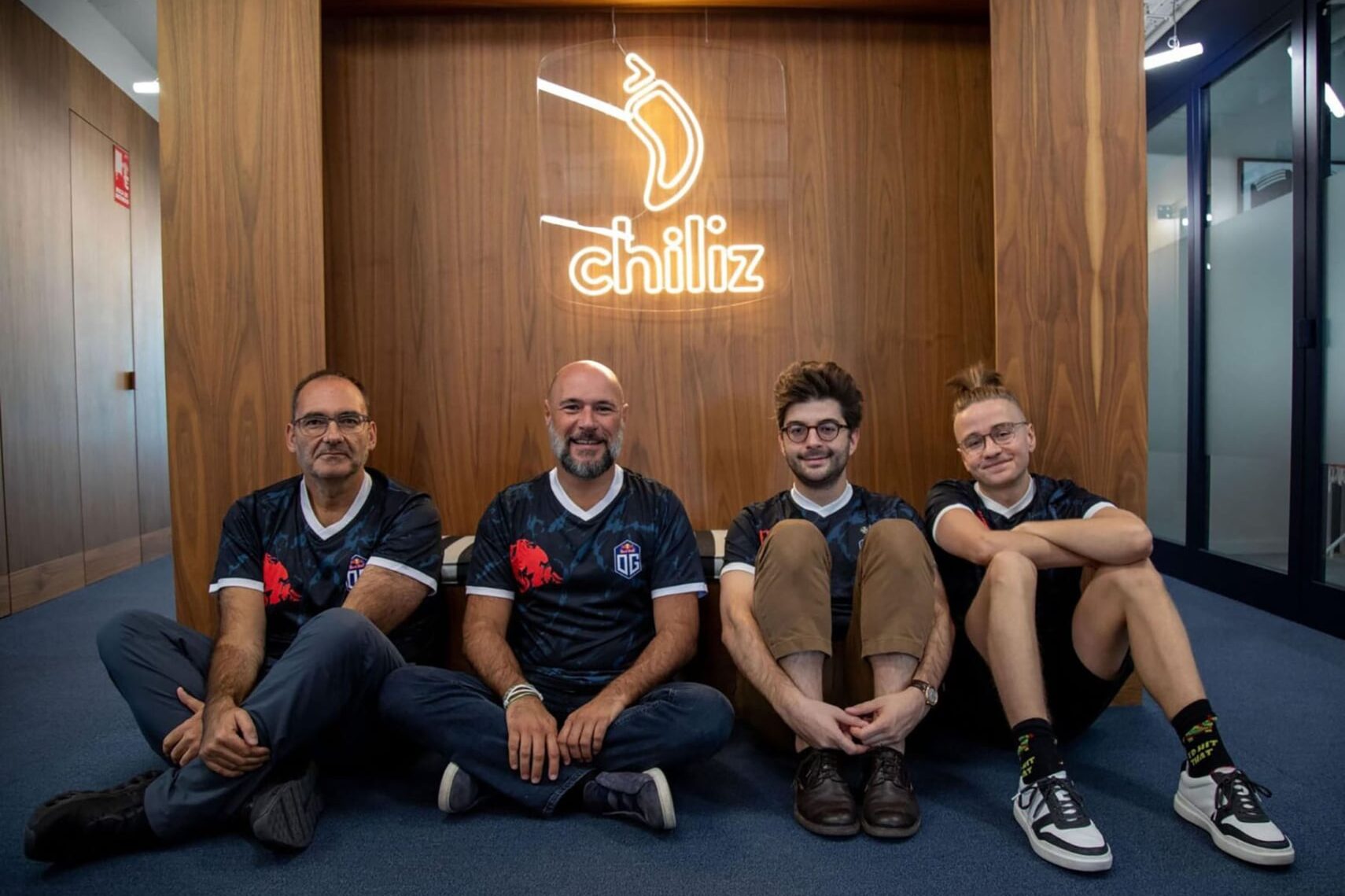 Image of people wearing OG Esports jerseys while sat near a wall displaying the Chiliz logo