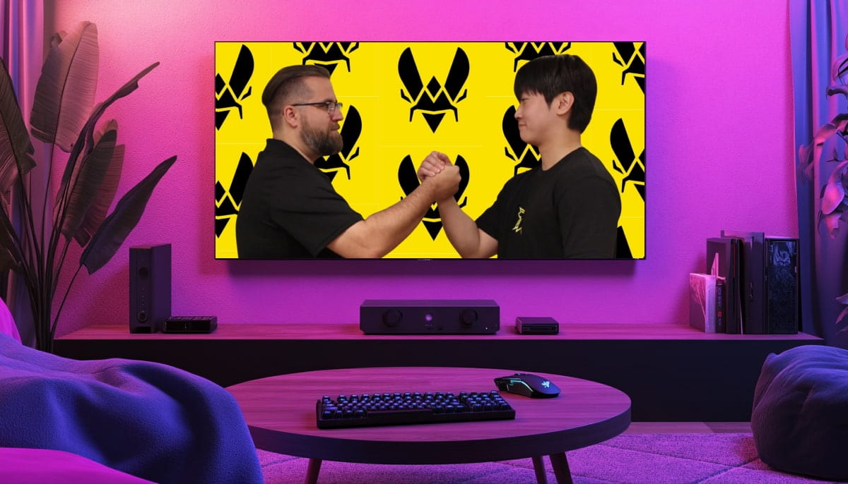 A cozy living room with pink lighting features a large screen showing two men in a handshake with serious expressions