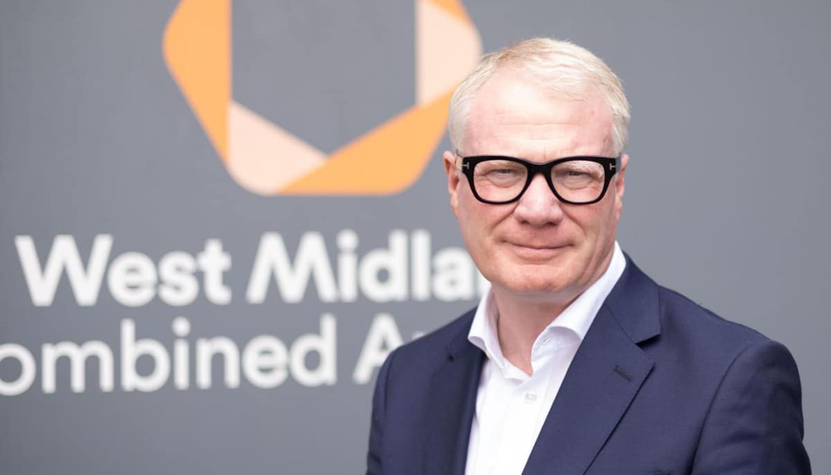 Richard Parker in a dark suit and glasses stands in front of a logo for "West Midlands Combined Authority"