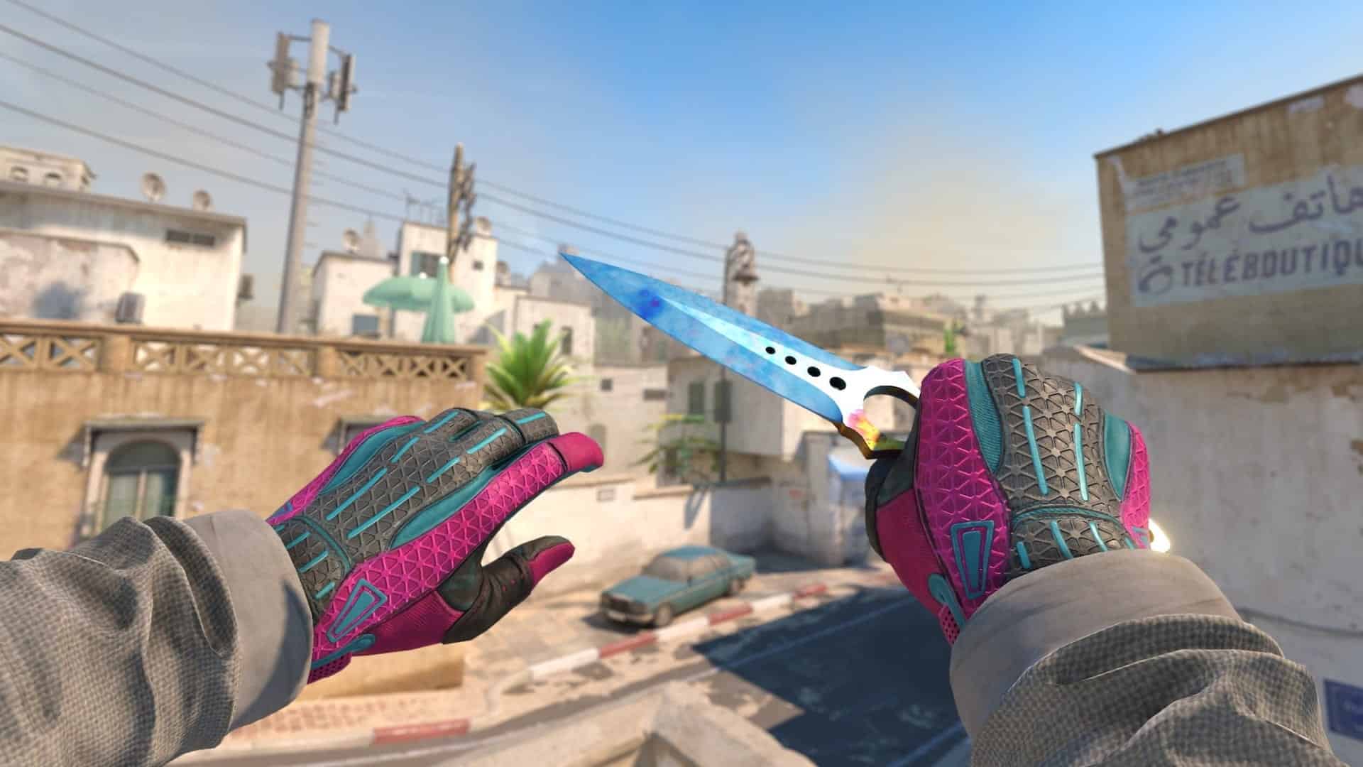 First-person view in CS 2, showing hands in pink and teal gloves holding a bright blue knife