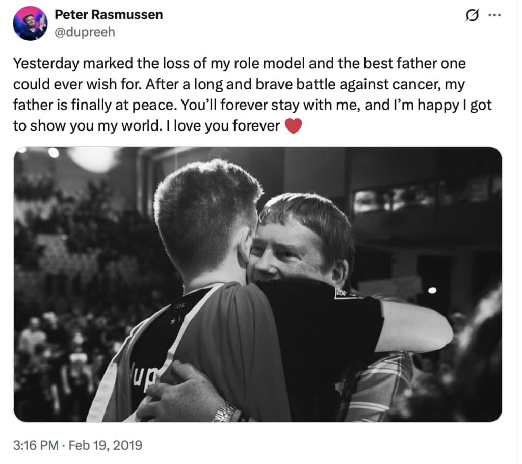 A black and white photo shows two people embracing warmly. The atmosphere is emotional and heartfelt, set against a blurred indoor background
