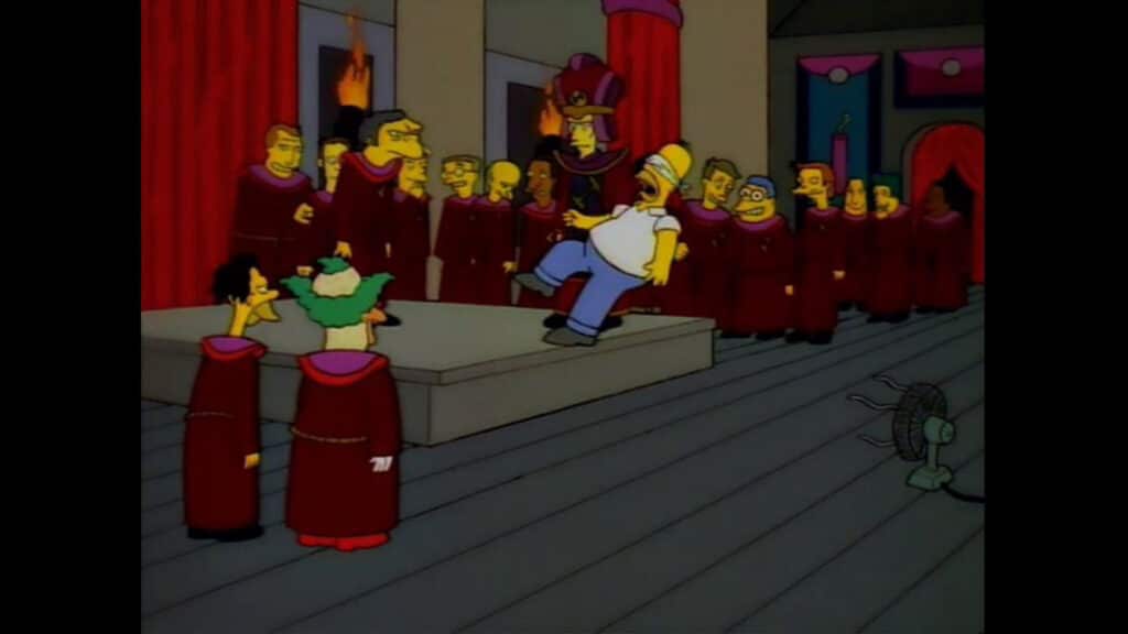 L'immagine mostra un fotogramma della serie animata “I Simpson”, in cui Homer Simpson è circondato da membri di una società segreta.