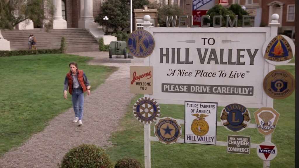 La scena del film Ritorno al futuro in cui Marty McFly appare mentre cammina lungo un sentiero verso un grande cartello che dice "Benvenuto a Hill Valley, un bel posto in cui vivere. Guida con prudenza!"