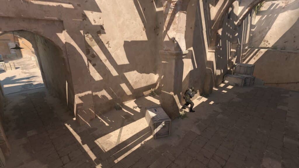 Das Bild zeigt eine taktische Position auf der Wettbewerbskarte „Dust II“ in Counter-Strike 2. Der spezifische Ort ist die Ecke in der Nähe des Tunnelausgangs (Tunnel/Höhle) zu Punkt B, wo sich der Spieler hinter einer Kiste (Höhle/Haus) verstecken kann.