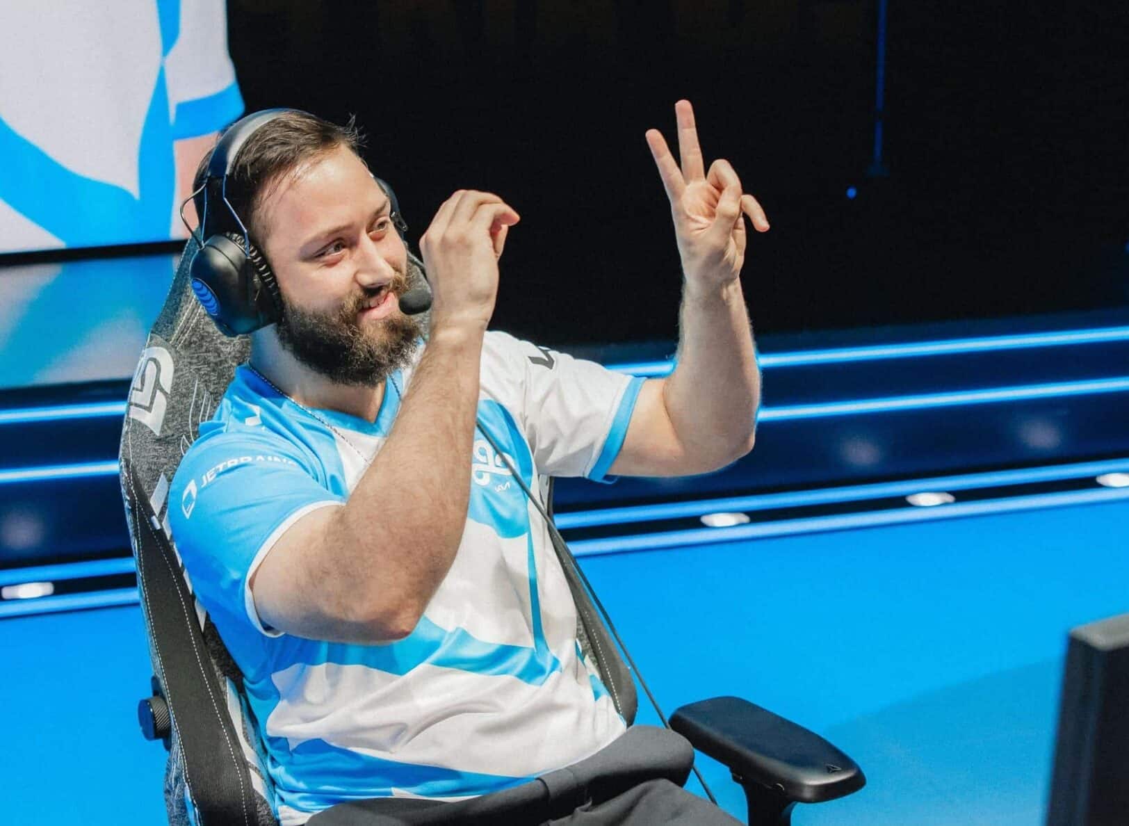 Ein lächelnder, bärtiger E-Sport-Spieler LemonNation, der ein blau-weißes Cloud9-Trikot und ein Headset trägt, macht während des Wettkampfs ein Friedenszeichen mit der Hand