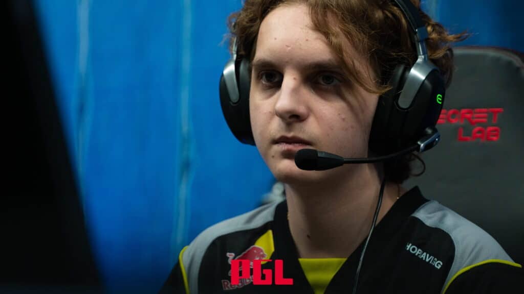 A young male esports player wearing a black and gray team jersey with Red Bull and NAVI logos, and a headset with a microphone