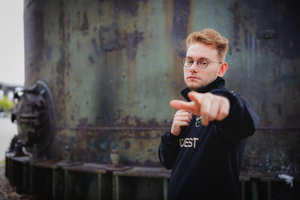 Inspiriert trägt er eine schwarze Jacke und eine Brille und zeigt in einer industriellen Umgebung auf die Kamera