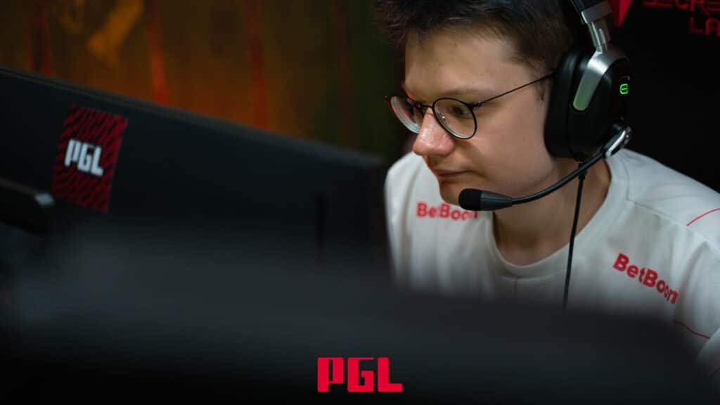 A professional e-sports player from the BetBoom team is wearing a headset and glasses while focused on a screen during a PGL tournament match
